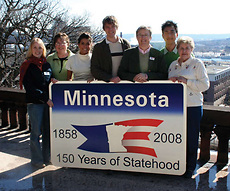 The Minnesota Sesquicentennial Commission poses with a sign outside its offices in St. Paul.