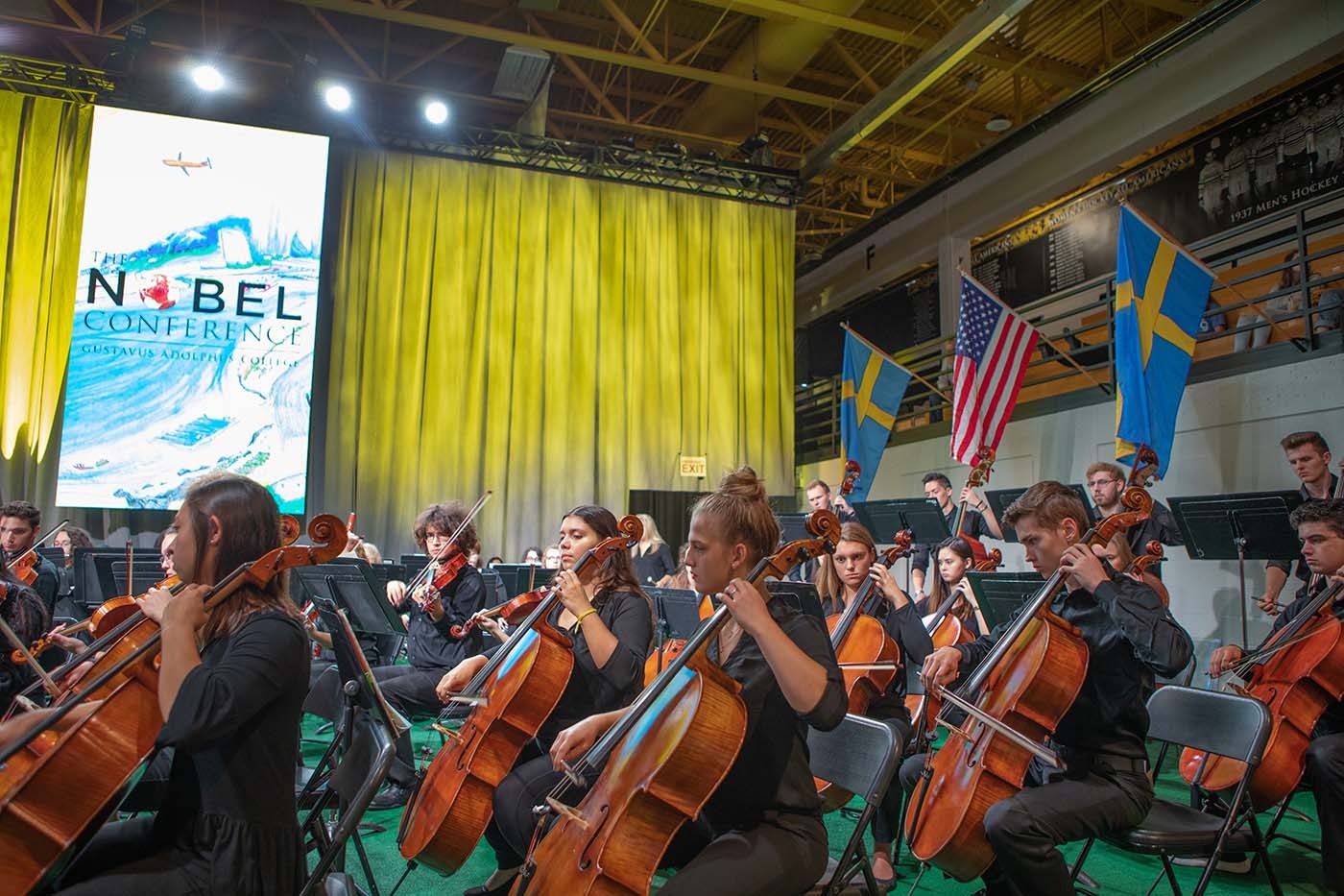 Students of Gustavus Orchestra, performing at Nobel Conference with stage in background.