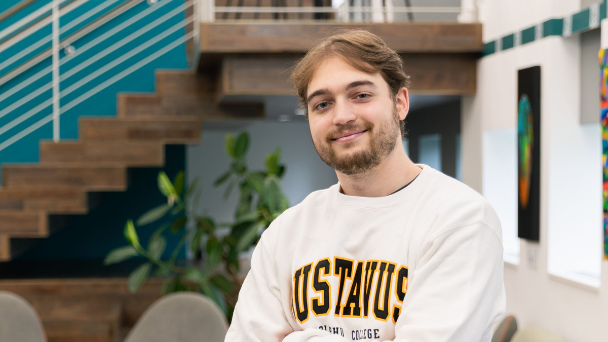 Student wearing white Gustavus sweater sitting and smiling into the camera.