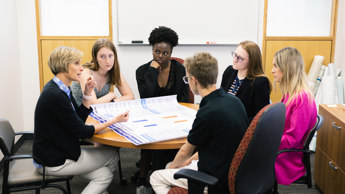 Image of students conversing with their professor around a table.