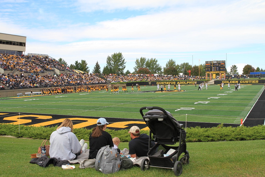 A family lays on the grass watching the Gustavus football game
