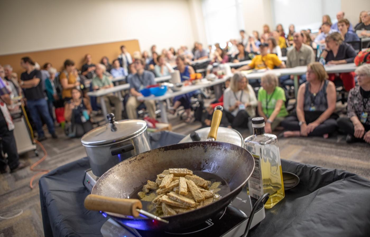 A pan of food is frying before a crowd. 