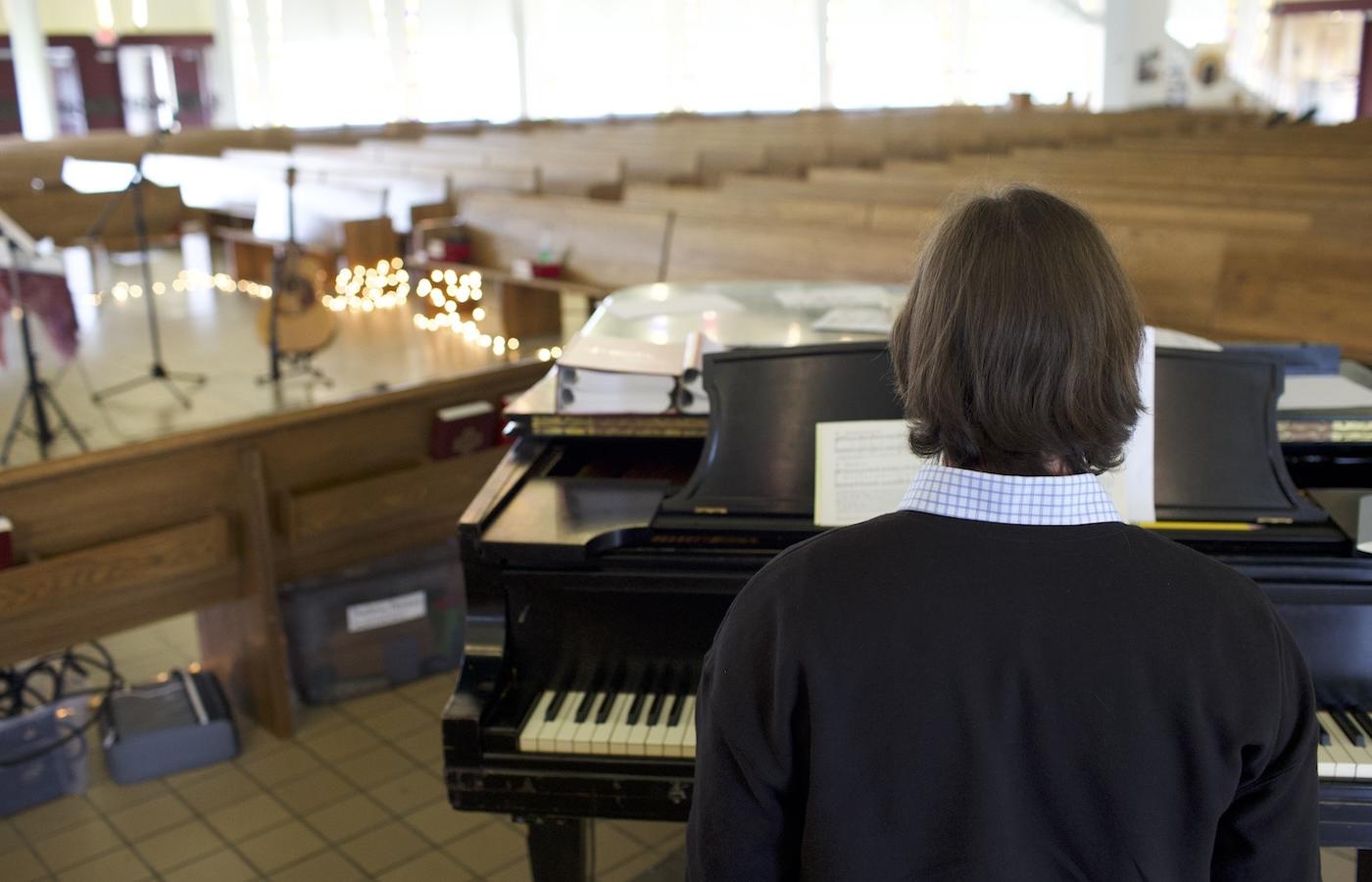 a student sits before a piano in a Chapel set for additional musicians. 