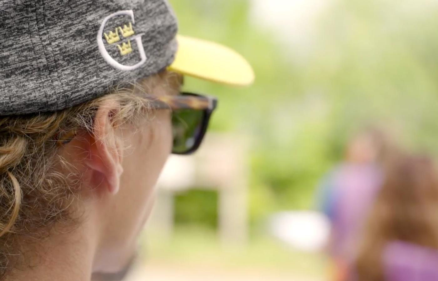 A young person in a Gustavus Adolphus College hat looks toward a bright future in sunglasses. 