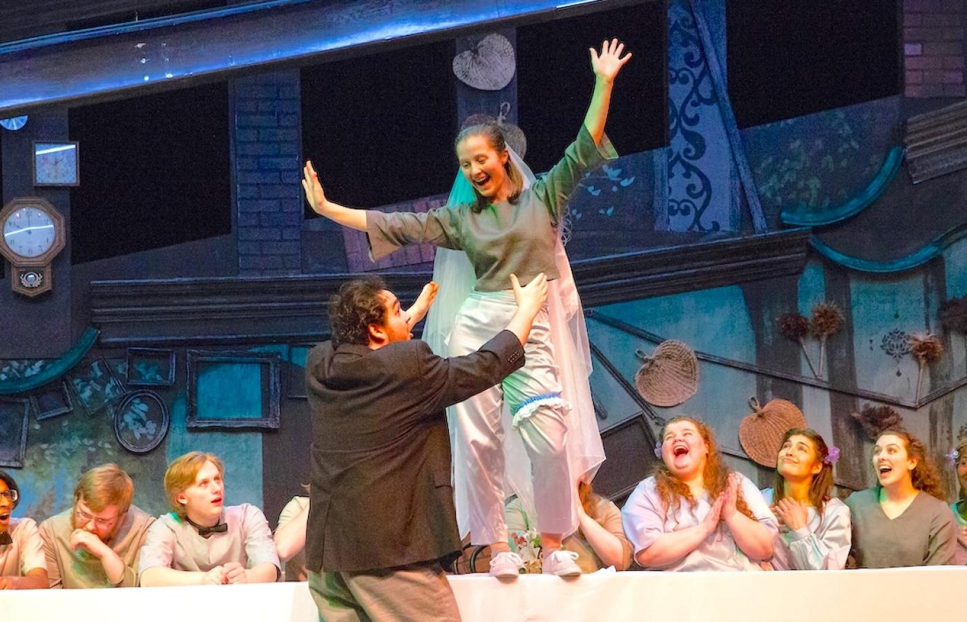 A student performer on a table leaps into her lovers arms while a table of guests claps. 