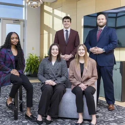Five professionally dressed students pose together in a modern office setting, representing the Gustavus Innovation Scholars program