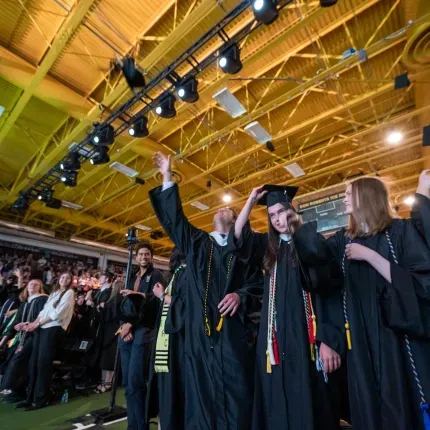 College students throw their hats up at a Commencement ceremony. 