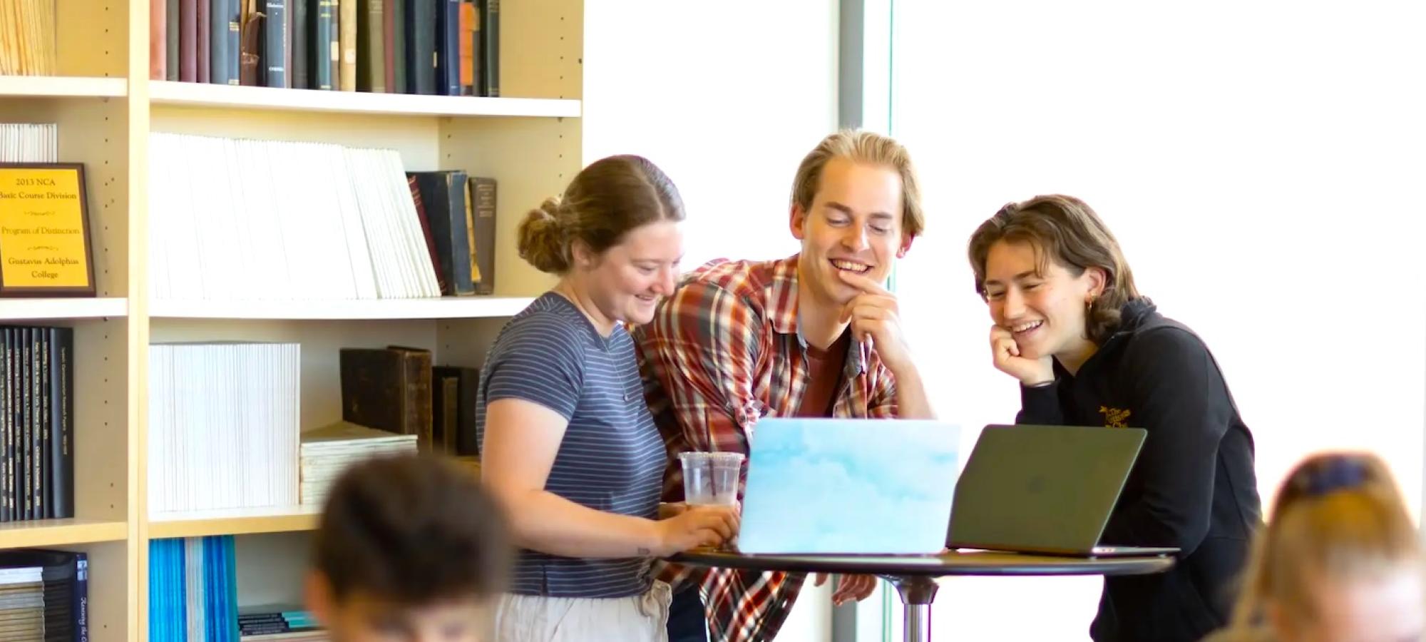 Three students work together in a sunny book-lined room. 