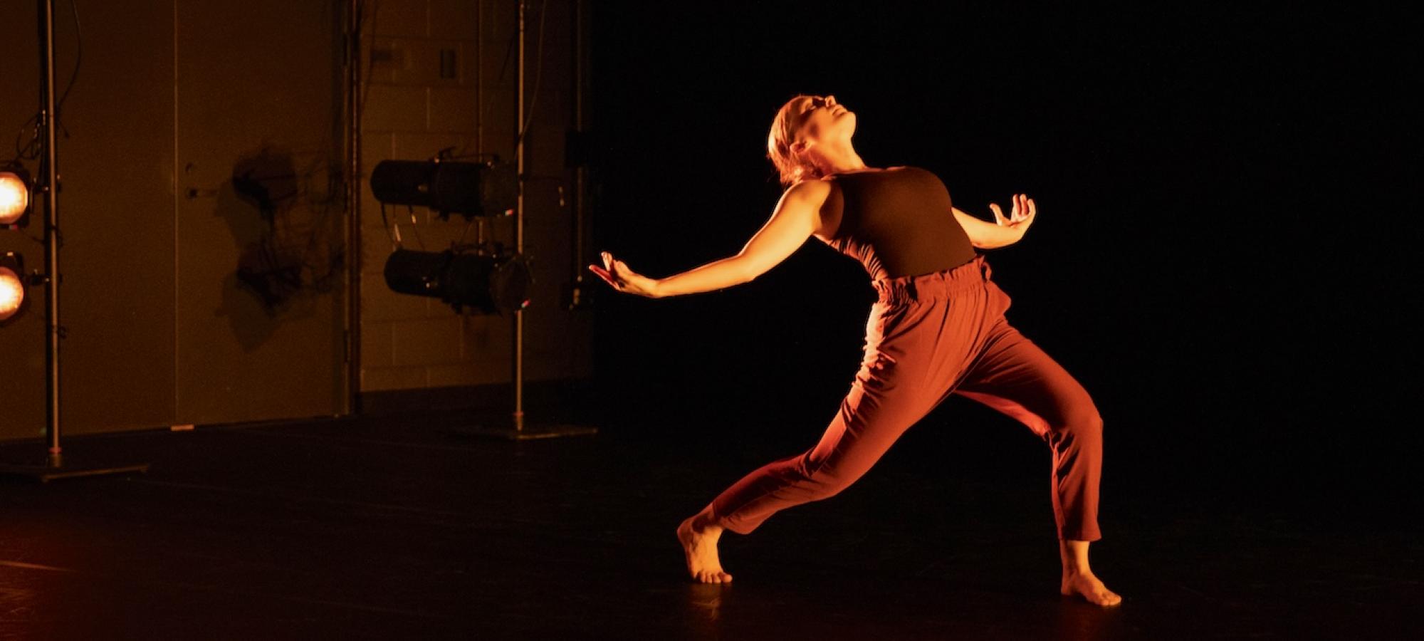 A woman dances dramatically in a black theater. 