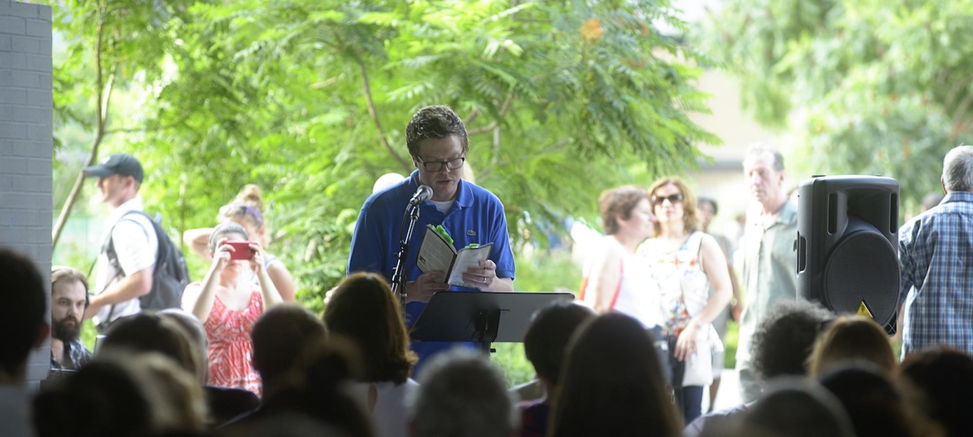 A man reads from his work to a crowd.