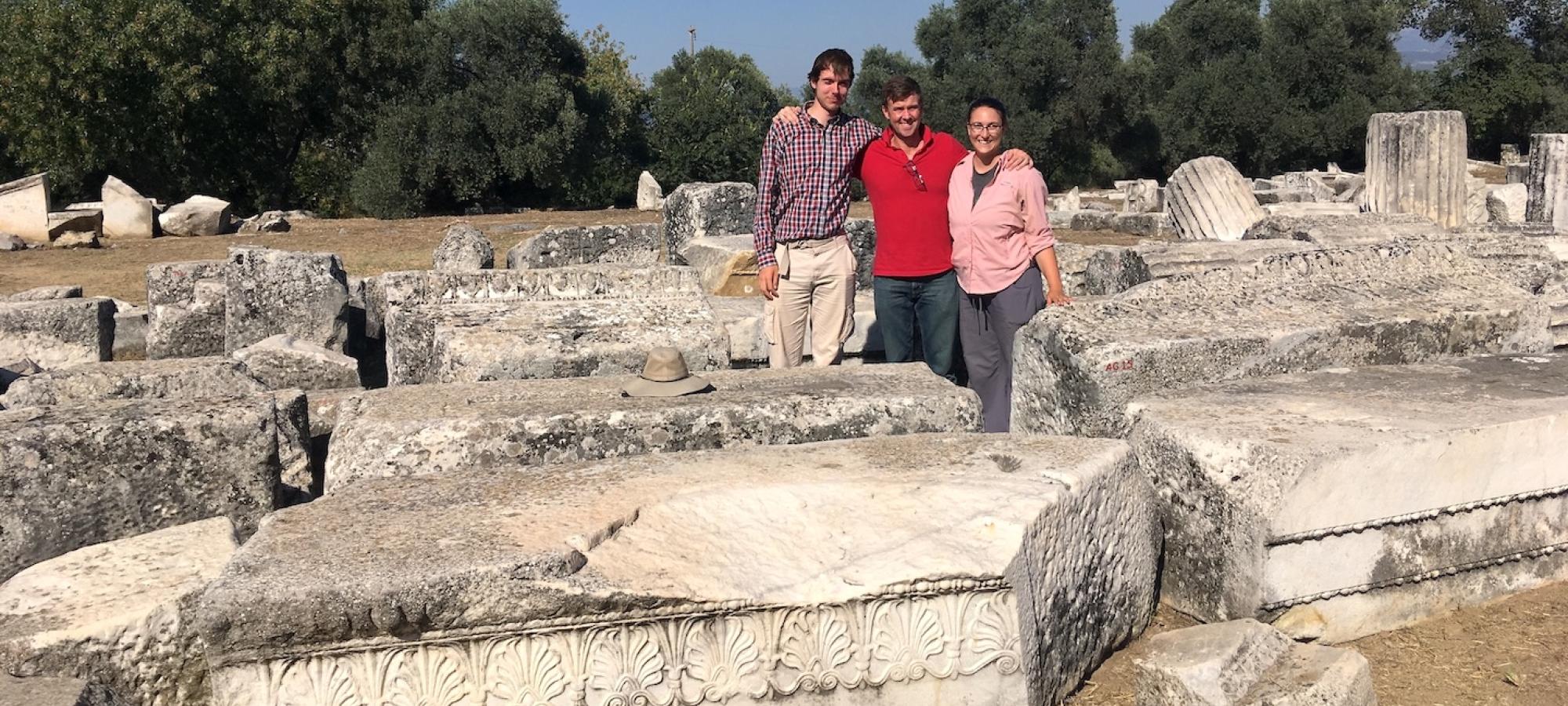A student and his professors stand among ancient ruins. 