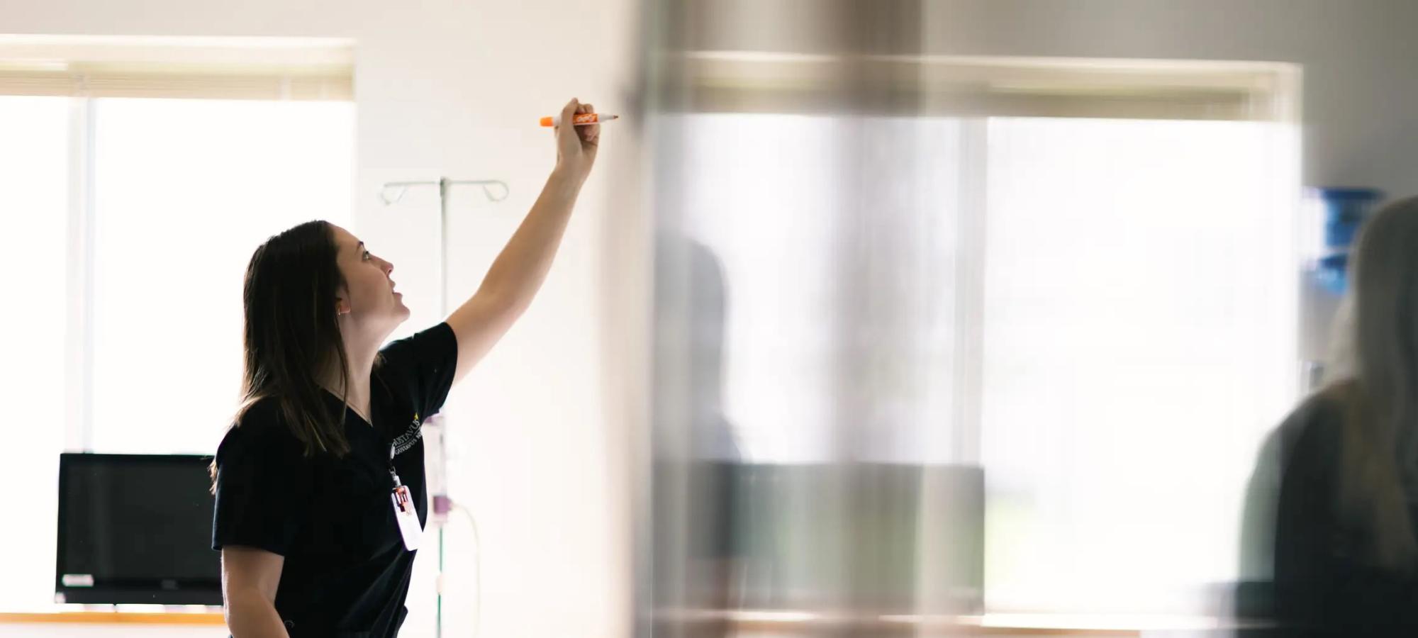 A Gustavus nursing students writes information on a whiteboard. 