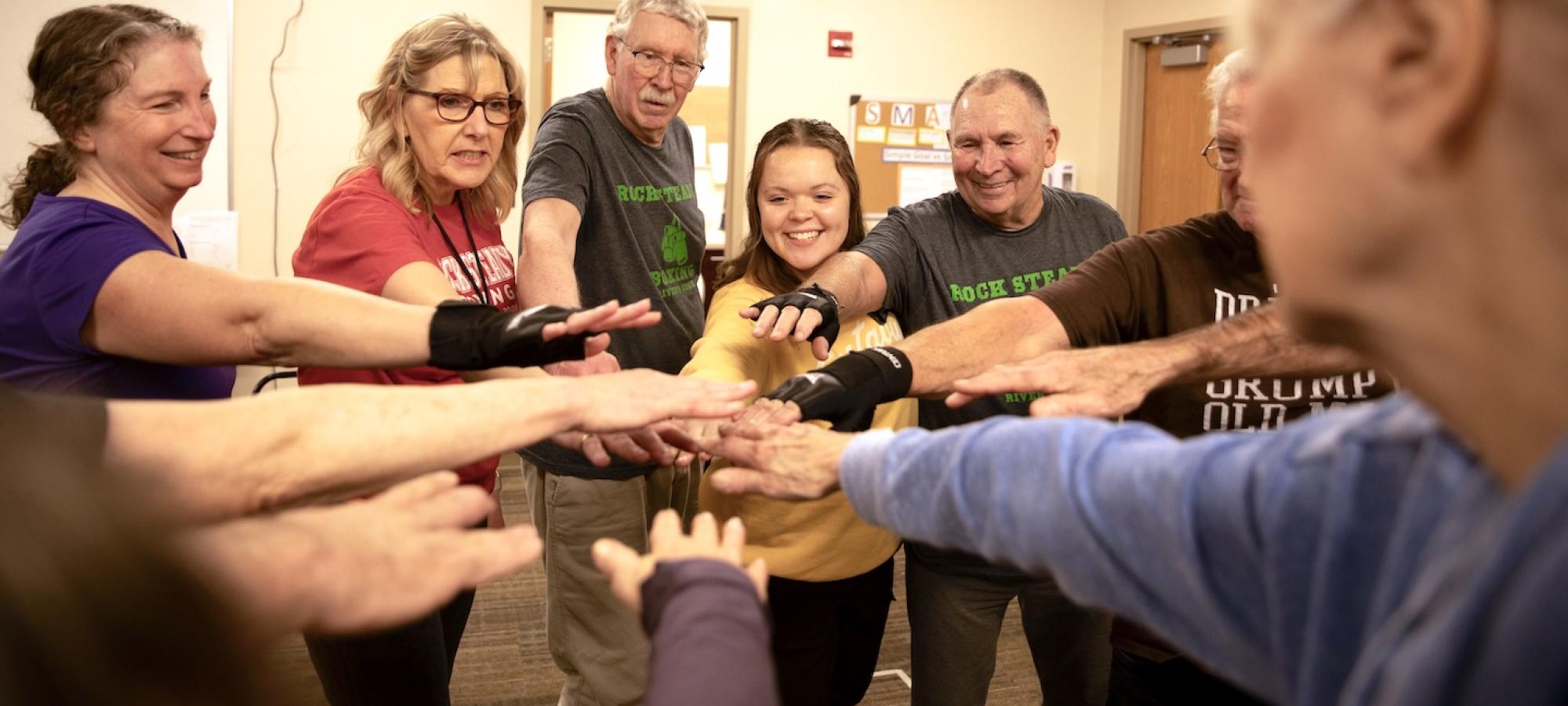 a group of multi-generational exercisers put their hands in a circle. 