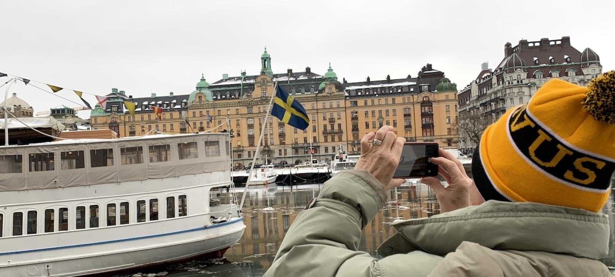 A person takes a photo of a boat with the Swedish flag. 