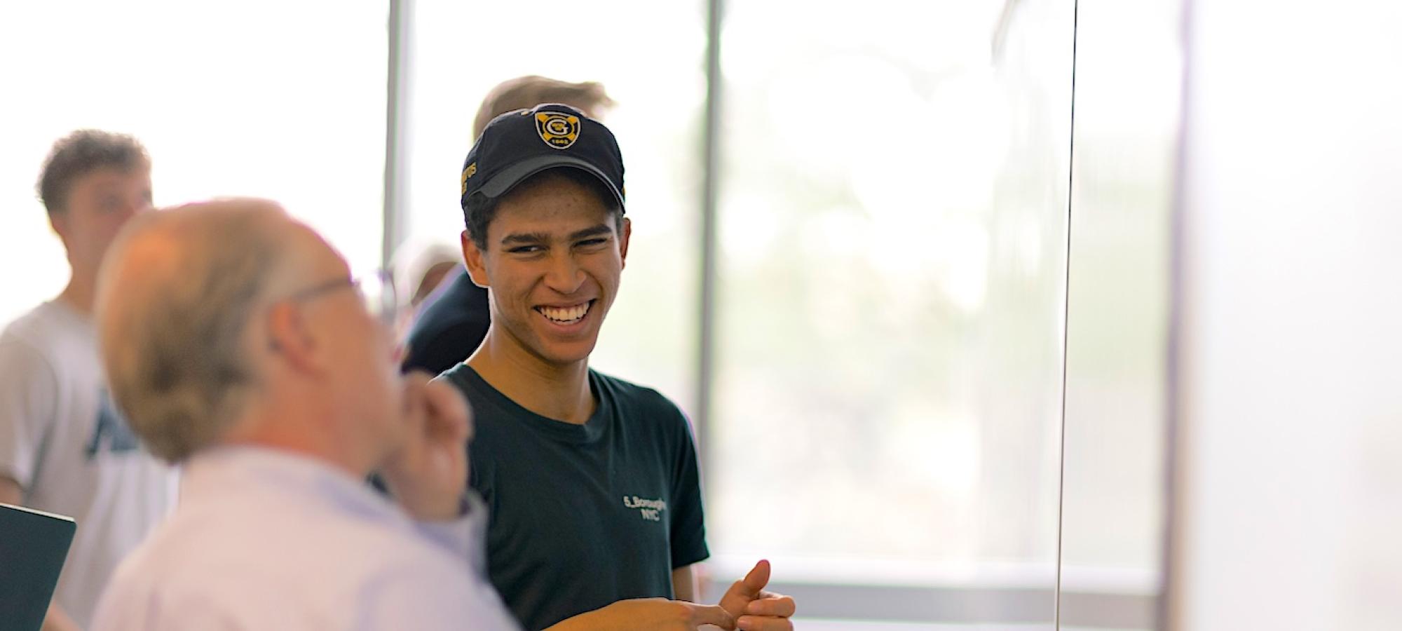 A student in a Gustavus Adolphus College golf hat looks at a professor and smiles. 