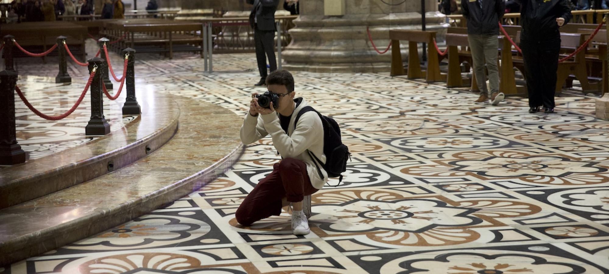 A student photographs while kneeling on an ornate cathedral floor. 