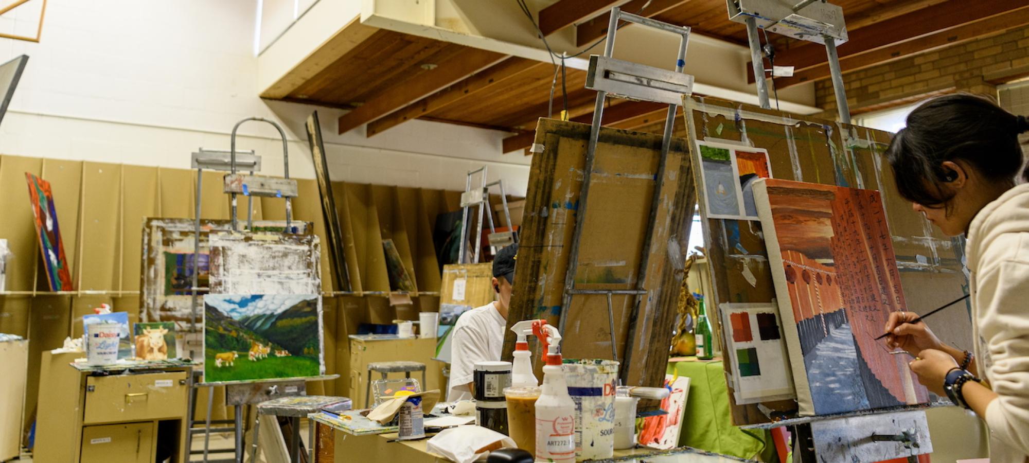 Students paint in a messy painting studio. 