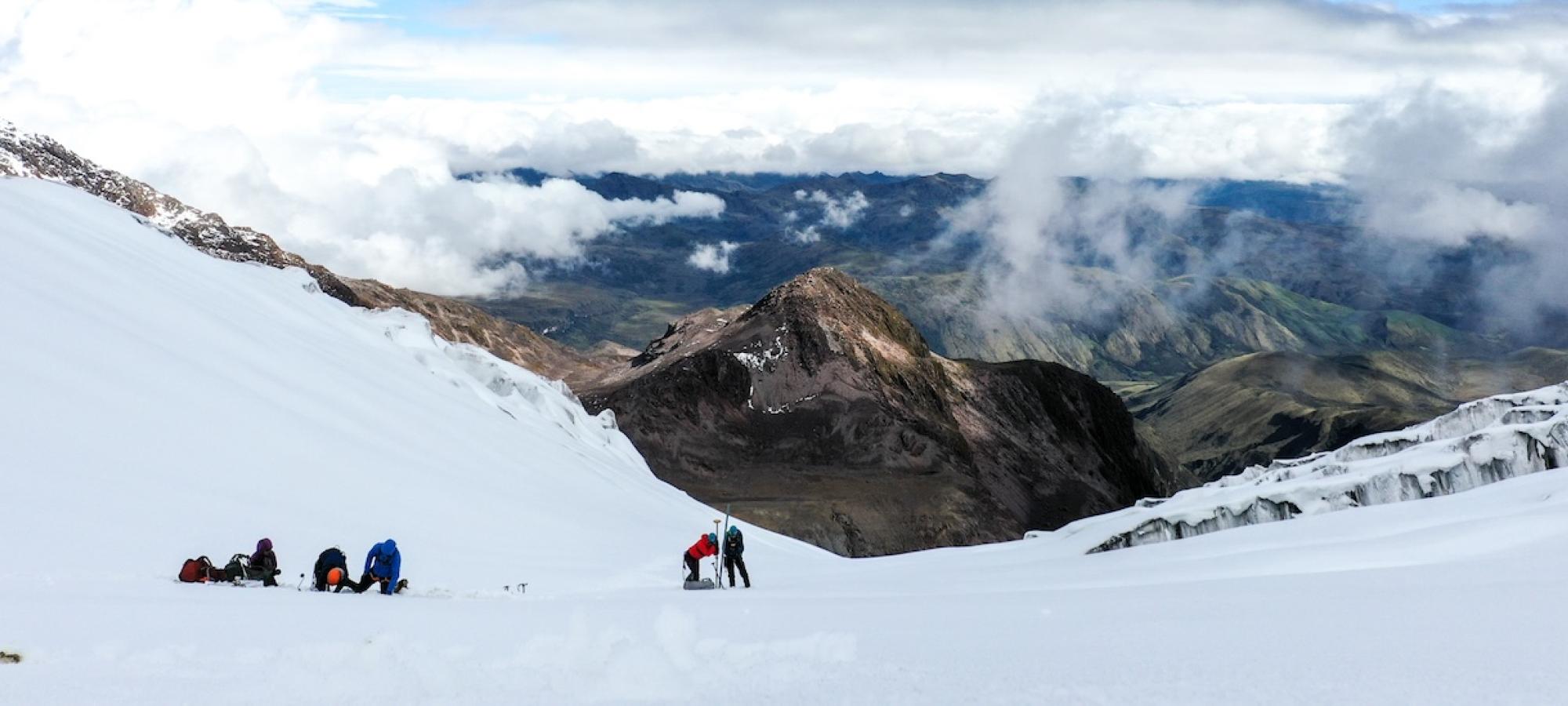 People on a mountain glacier set up equipment against a green landscape.