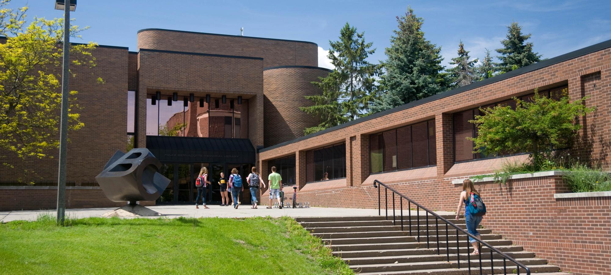 Students walking into Folke Bernadotte Library with Sculpture in foreground