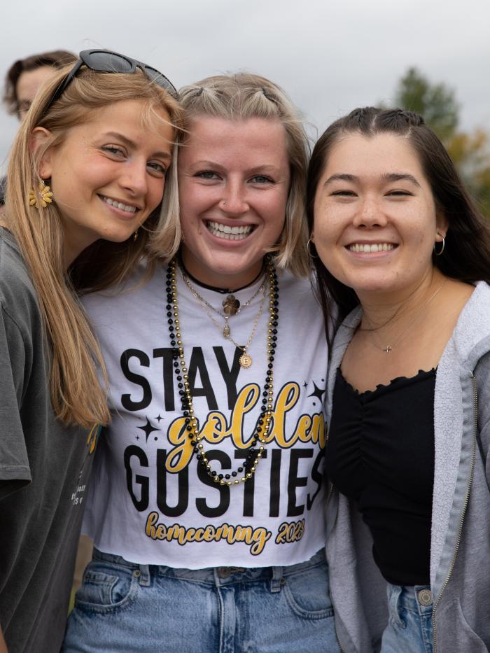 Three students in college Homecoming dress smile for the camera. 