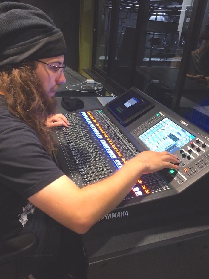 A student handles the digital controls of a large performance audio visual console. 